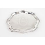 A GEORGE III SILVER TEAPOT STAND of shaped oval form, the centre with engraved crest, on four