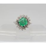 AN EMERALD & DIAMOND CLUSTER RING set with a 6.1mm x 6.4mm x 4.4mm step cut emerald, and estimated