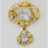 AN ARTS & CRAFTS PENDANT BROOCH mounted in yellow metal, and set with two aquamarines, largest