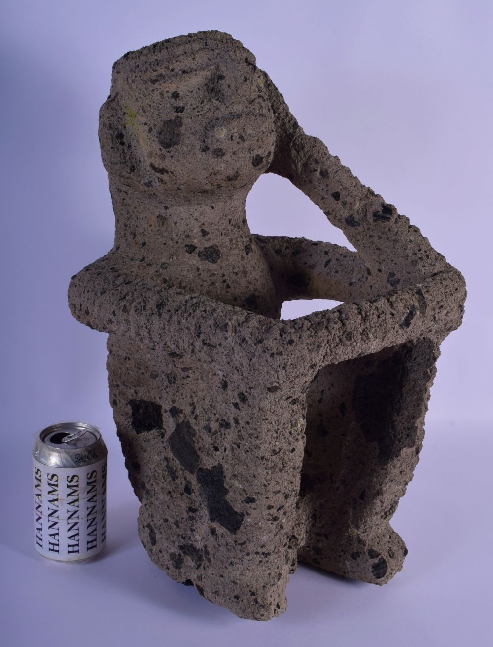 A LARGE SOUTH AMERICAN VOLCANIC STONE FIGURE OF A SEATED MALE possibly Peruvian, modelled clutching