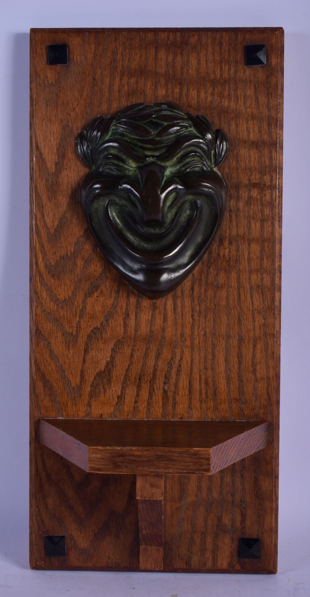 A CHARMING ARTS AND CRAFTS BRONZE MOUNTED OAK WALL PLINTH formed with a theatrical mask head. 40 cm