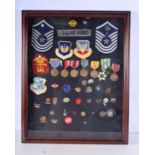 A framed collection of American military badges, medals and enamelled badges 55 x 46 cm.