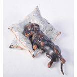 A COLD PAINTED BRONZE FIGURE OF A DACHSHUND LYING ON PILLOWS. 9.5cm x 5.6cm x 2.8cm, weight 283.6g