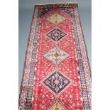 A QASHQAI WOOL RUNNER, modern, the claret red floral field with five diamond shaped guls in navy