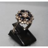 A SAPPHIRE AND DIAMOND CLUSTER RING claw set with six round facet cut claw set sapphires within a