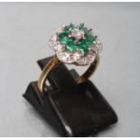 AN EMERALD AND DIAMOND CLUSTER RING, with six round facet cut emeralds claw set to a border of