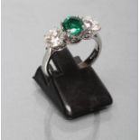 AN EMERALD AND DIAMOND THREE STONE RING, the central circular facet cut emerald flanked by two round