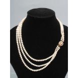 A TRIPLE STRAND CULTURED PEARL NECKLACE, the graduated pearls on a flowerhead clasp, stamped 9ct (