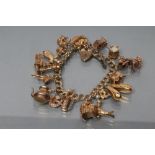 A 9CT GOLD DOUBLE CURB LINK BRACELET, London 1965, hung with eighteen charms, 64.6g gross (Est. plus