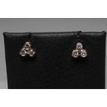 A PAIR OF DIAMOND EAR STUDS, each open back collet set with three small stones to plain white posts,