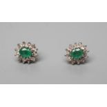 A PAIR OF EMERALD AND DIAMOND CLUSTER EAR STUDS, the central facet cut emerald to a border of twelve