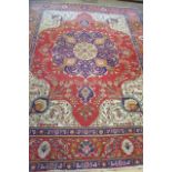 A PERSIAN WOOL RUG, the red floral field with similar navy blue and ivory central gul