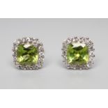 A PAIR OF PERIDOT AND DIAMOND CLUSTER EAR STUDS, the square facet cut peridot within a border of