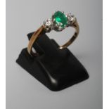 A THREE STONE EMERALD AND DIAMOND RING, the central oval facet cut emerald claw set and flanked by