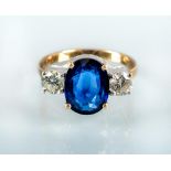 A THREE STONE SAPPHIRE AND DIAMOND RING, the oval facet cut sapphire flanked by two round