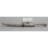 AN INDIAN DAGGER, with 6 1/2" blade, floral decorated grip and white metal embossed sheath depicting