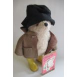 A Paddington bear, with brown coat, black hat and yellow dunlop boots, together with a Puffin