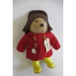 A Paddington bear, with amber eyes, plastic nose, felt red coat, yellow Dunlop boots, Brown hat