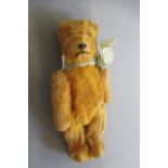 A miniature straw filled teddy, with one amber eye, sewn nose, hinged joints and orange plush, 5 7/