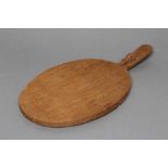 A ROBERT THOMPSON ADZED OAK CHEESE BOARD of oval form, carved mouse trademark in high relief to