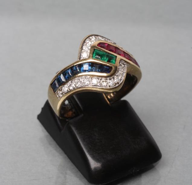 A RUBY, SAPPHIRE AND EMERALD DRESS RING. the channel set calibre cut stones within point set diamond