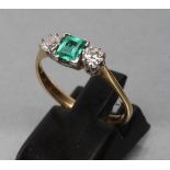 AN EMERALD AND DIAMOND THREE STONE RING, centred by a square cut emerald claw set and flanked by two