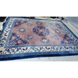 A CHINESE WASHED AND FRINGED CARPET, the dusky pink field with central floral gul in shades of blue,