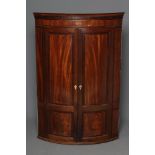 A GEORGIAN MAHOGANY CORNER CUPBOARD, c. 1800, of bowed form with rosewood banding and stringing,