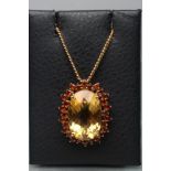 A CITRINE PENDANT, the all-over facet cut oval central stone claw set to a border of small darker