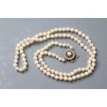 A SINGLE STRING OF CULTURED PEARLS, with split pearl and emerald chip 9ct gold flower clasp,