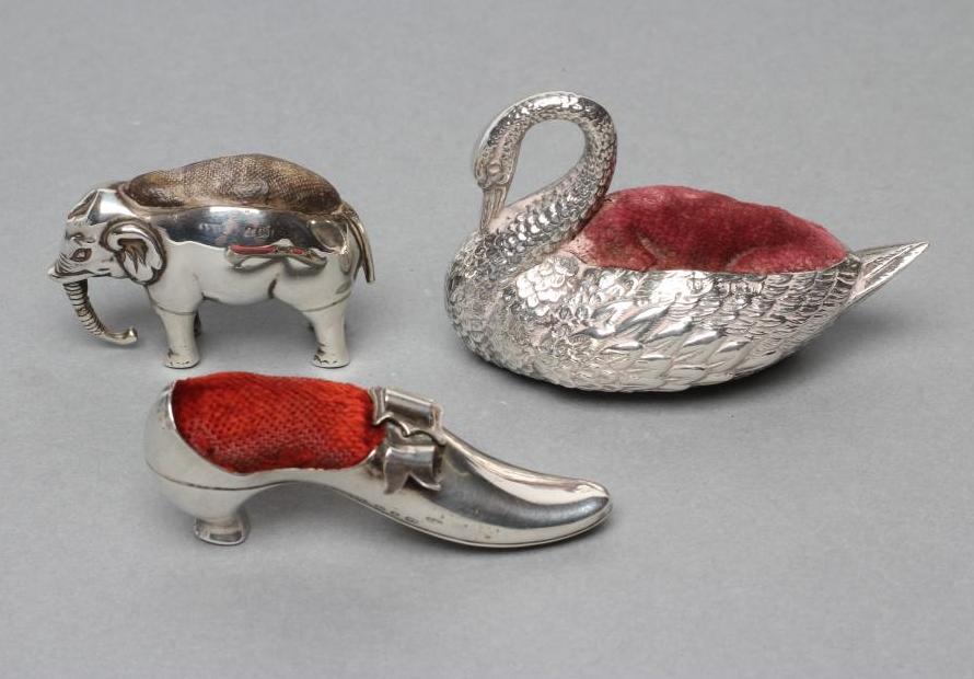 THREE NOVELTY SILVER PIN CUSHIONS comprising a shoe with bow and buckle on a Louis heel,