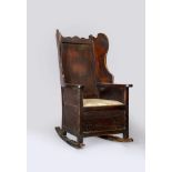 AN OAK LAMBING CHAIR, early 19th century, the winged and panelled back with scrolled crest rail,
