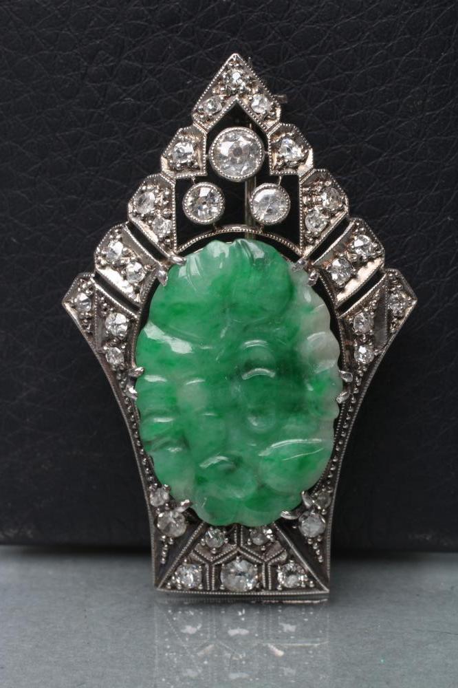 AN ART DECO JADE AND DIAMOND BROOCH, the oval green jade panel carved with fruits and claw set to