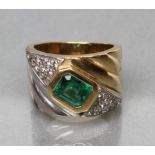 AN EMERALD COCKTAIL RING, the facet cut square emerald collet set in yellow gold between two