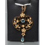 AN EDWARDIAN PENDANT, stamped 15ct, of open scroll form centred by a circular facet cut aquamarine