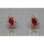 A PAIR OF RUBY AND DIAMOND EAR STUDS, the facet pear cut ruby claw set to a border of small round