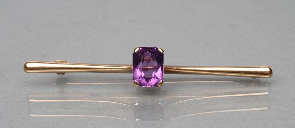 AN EDWARDIAN PROPELLOR BAR BROOCH centred by an oblong facet cut amethyst, stamped 9ct (Est. plus