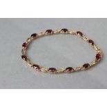 A GARNET BRACELET, the twelve oval facet cut stones claw set to a plain chain, stamped 375 (Est.