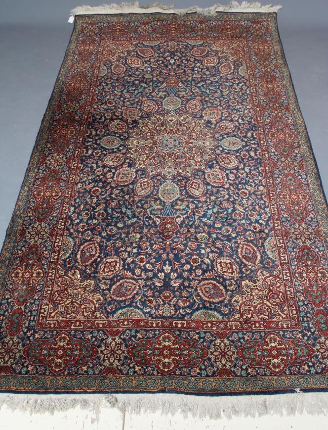 A PERSIAN RUG, the navy blue floral field centred by an ivory circular gul with matching