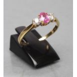 A PINK SAPPHIRE AND DIAMOND THREE STONE RING, the oval facet cut sapphire claw set and flanked by