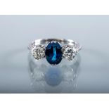 A SAPPHIRE AND DIAMOND THREE STONE RING, the central facet cut oval sapphire claw set and flanked by