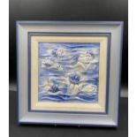 A Moorcroft framed blue and white relief tile depicting faces and hands in waves. Frame 32.5 x 32.