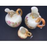 Three Royal Worcester blush ivory jugs with beak spouts and C scroll strap handles decorated with