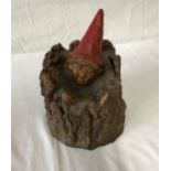Gnome sat in the base of a tree. Height 22cms, diameter 18cms.Condition ReportAmateur repair, scuffs