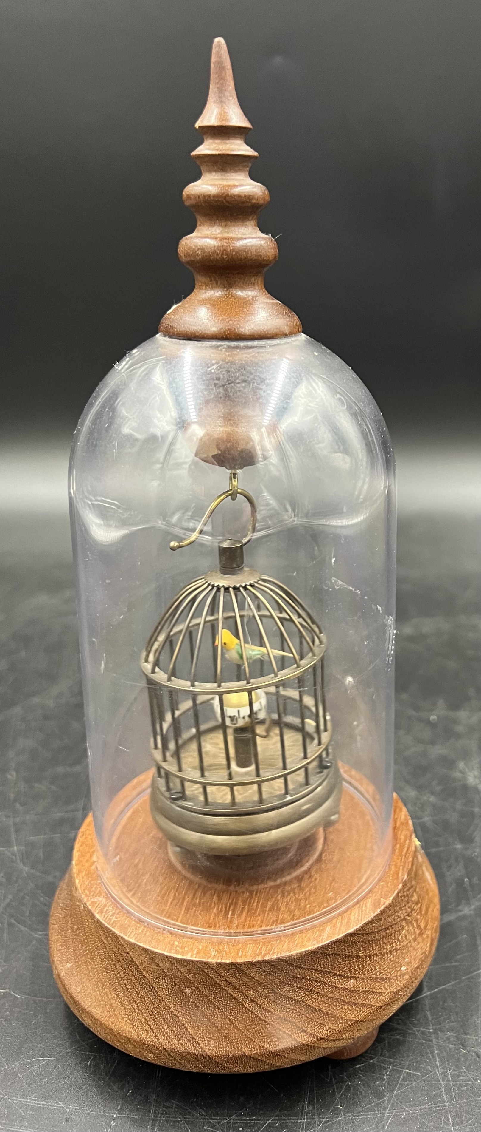 A novelty clock displayed under a clear dome on a wooden base. The vintage style metal birdcage