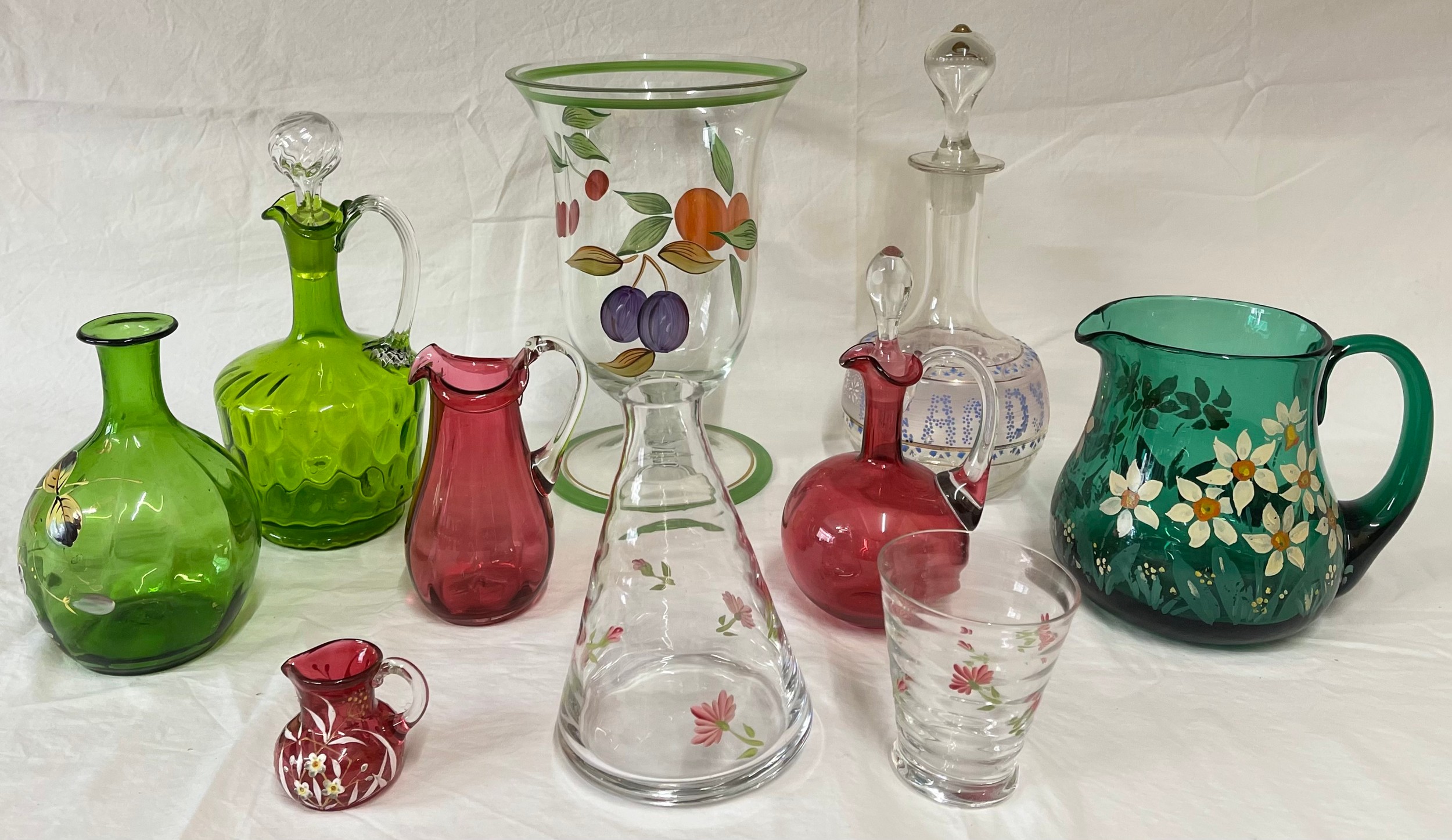 A selection of coloured and hand painted glass ware to include: 3 x cranberry jugs, 3 x green jugs