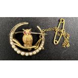 A 15ct crescent shaped brooch with an owl on branch, set with seed pears and rubies with safety