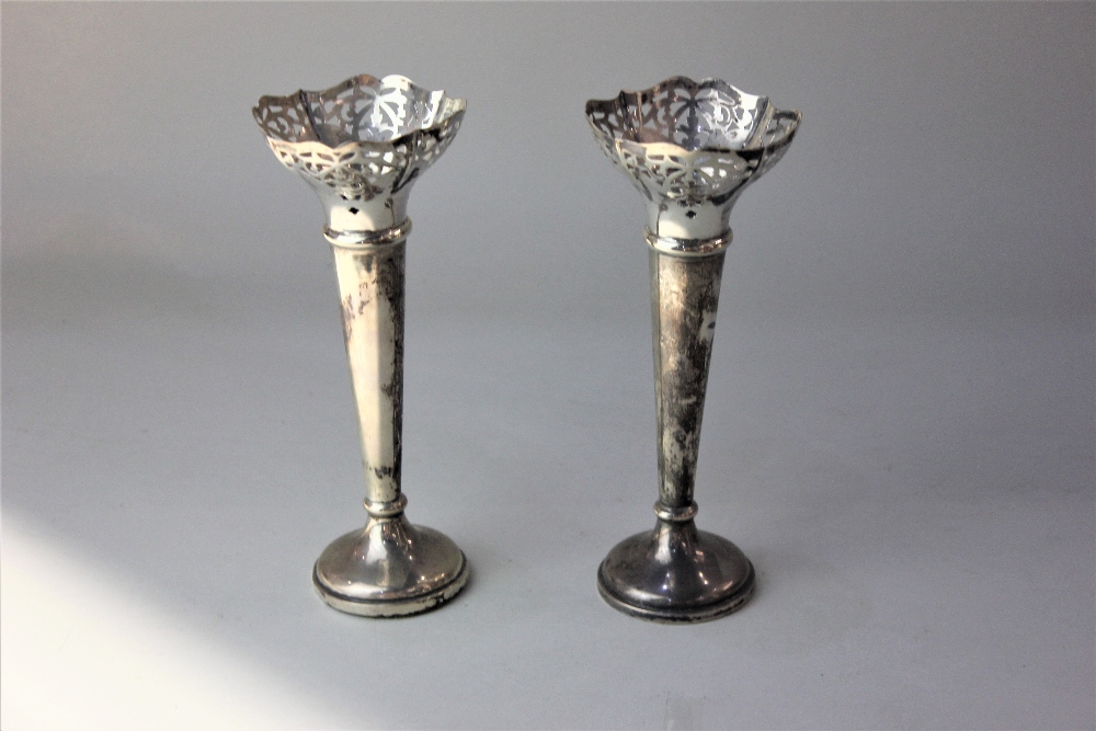 A pair of George V silver vases with pierced rims on tapered stems and loaded circular bases, (af)