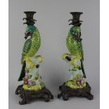 A pair of continental gilt metal mounted porcelain parrot candlesticks perched on stumps with