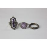 A silver mounted dress ring set with three oval cuts; a step cut amethyst dress ring between two